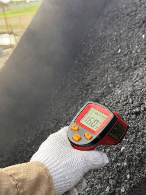 Mano con guante midiendo con termómetro infrarrojo la temperatura de la mezcla asfáltica