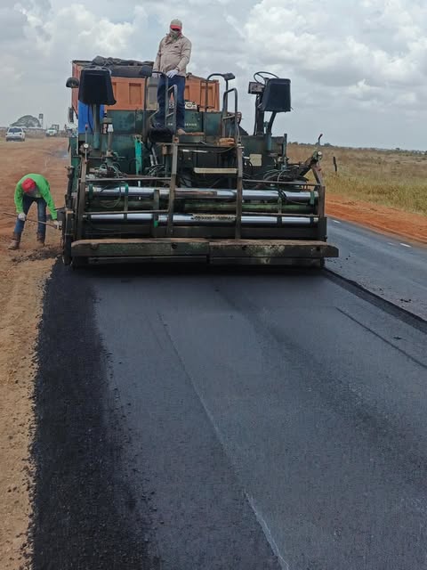 Pavimentadora tendiendo mezcla asfáltica sobre una vía nueva con una cuadrilla en obra